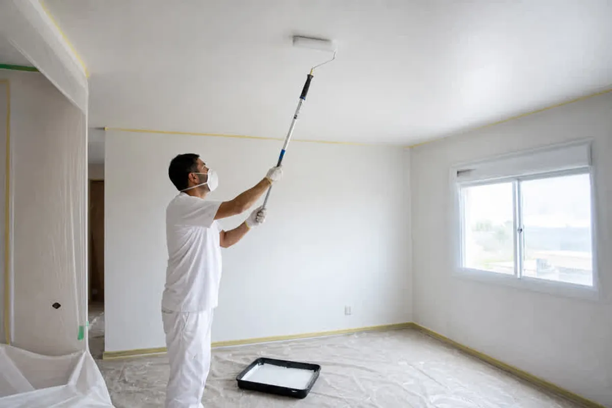Pintor predial realizando pintura de teto e forro com rolo extensor e piso protegido