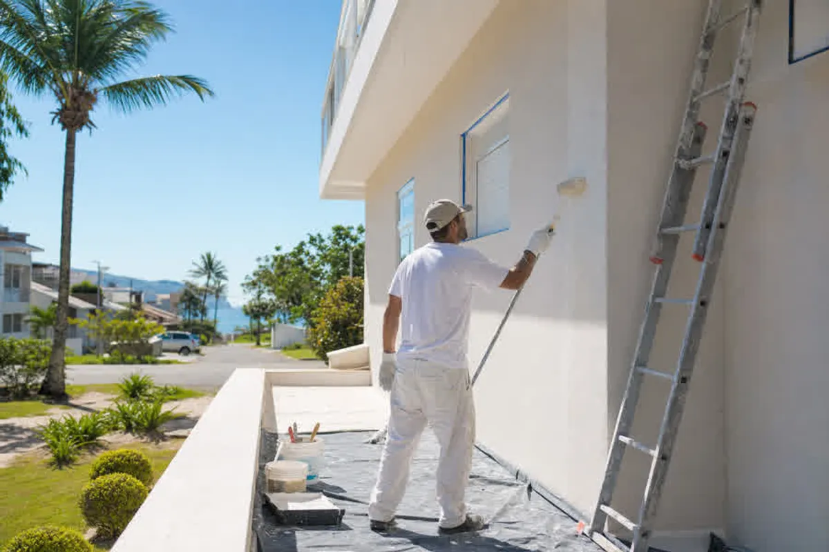 Pintor profissional aplicando tinta na parede externa de uma casa no Rio Tavares