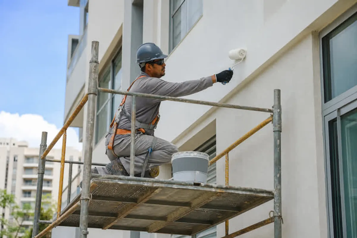 Pintor profissional pintando a fachada de um predio residencial sobre andaime no Sertao do Peri